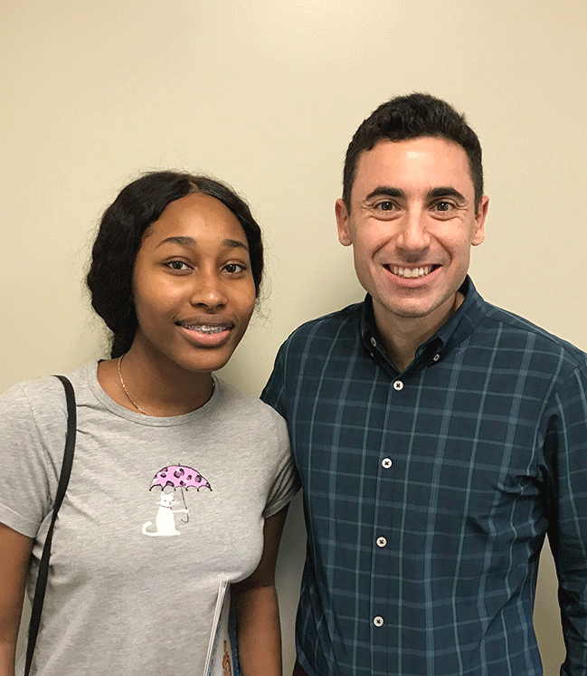 Young girl smiling wearing a grey tshirt standing next to a man also smiling wearing a plaid button down